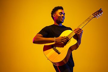 Image showing Young african-american musician singing, playing guitar in neon light