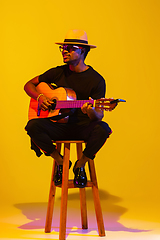 Image showing Young african-american musician singing, playing guitar in neon light