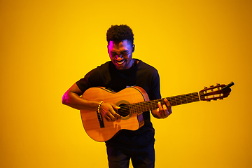 Image showing Young african-american musician singing, playing guitar in neon light