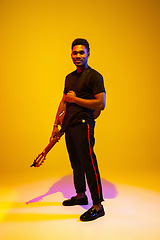 Image showing Young african-american musician singing, playing guitar in neon light