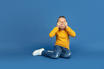 Image showing Portrait of sad little girl sitting on blue studio background, autism concept