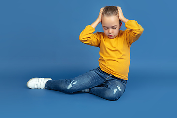 Image showing Portrait of sad little girl sitting on blue studio background, autism concept