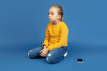 Image showing Portrait of sad little girl sitting on blue studio background, autism concept