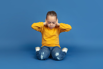 Image showing Portrait of sad little girl sitting on blue studio background, autism concept