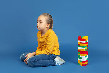 Image showing Portrait of sad little girl sitting on blue studio background, autism concept