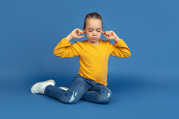 Image showing Portrait of sad little girl sitting on blue studio background, autism concept