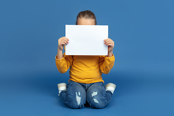 Image showing Portrait of sad little girl sitting on blue studio background, autism concept