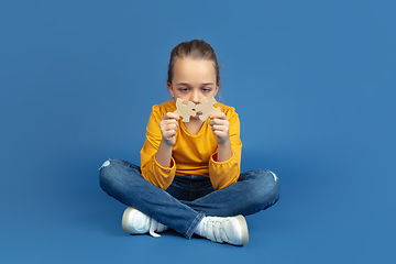 Image showing Portrait of sad little girl sitting on blue studio background, autism concept