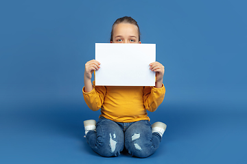 Image showing Portrait of sad little girl sitting on blue studio background, autism concept