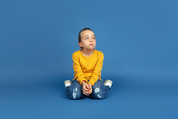 Image showing Portrait of sad little girl sitting on blue studio background, autism concept