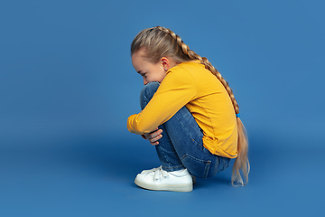 Image showing Portrait of sad little girl sitting on blue studio background, autism concept