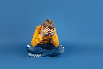 Image showing Portrait of sad little girl sitting on blue studio background, autism concept