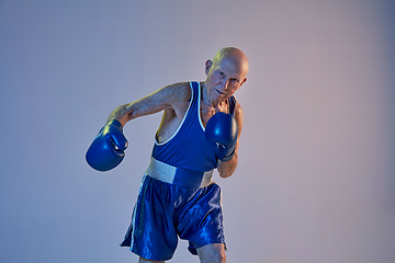 Image showing Senior man wearing sportwear boxing isolated on gradient studio background in neon light. Concept of sport, activity, movement, wellbeing. Copyspace, ad.