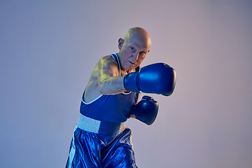 Image showing Senior man wearing sportwear boxing isolated on gradient studio background in neon light. Concept of sport, activity, movement, wellbeing. Copyspace, ad.