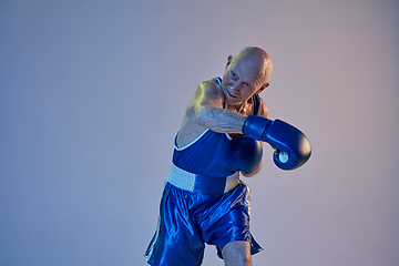 Image showing Senior man wearing sportwear boxing isolated on gradient studio background in neon light. Concept of sport, activity, movement, wellbeing. Copyspace, ad.