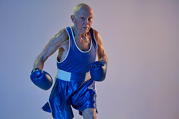 Image showing Senior man wearing sportwear boxing isolated on gradient studio background in neon light. Concept of sport, activity, movement, wellbeing. Copyspace, ad.