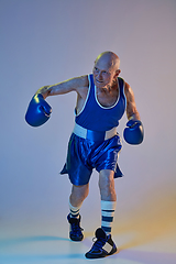 Image showing Senior man wearing sportwear boxing isolated on gradient studio background in neon light. Concept of sport, activity, movement, wellbeing. Copyspace, ad.