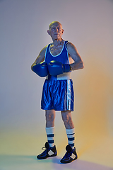 Image showing Senior man wearing sportwear boxing isolated on gradient studio background in neon light. Concept of sport, activity, movement, wellbeing. Copyspace, ad.