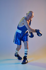 Image showing Senior man wearing sportwear boxing isolated on gradient studio background in neon light. Concept of sport, activity, movement, wellbeing. Copyspace, ad.