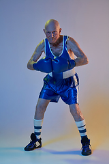 Image showing Senior man wearing sportwear boxing isolated on gradient studio background in neon light. Concept of sport, activity, movement, wellbeing. Copyspace, ad.