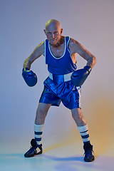 Image showing Senior man wearing sportwear boxing isolated on gradient studio background in neon light. Concept of sport, activity, movement, wellbeing. Copyspace, ad.