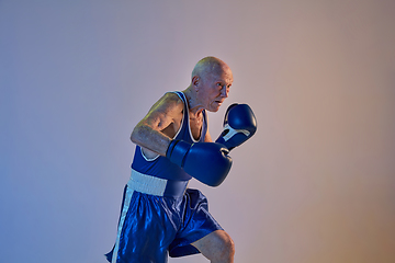 Image showing Senior man wearing sportwear boxing isolated on gradient studio background in neon light. Concept of sport, activity, movement, wellbeing. Copyspace, ad.