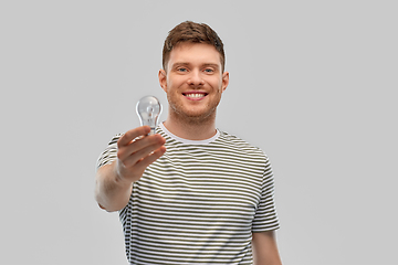 Image showing happy smiling young man holding light bulb