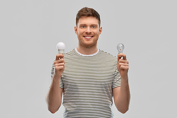 Image showing smiling young man comparing different light bulbs