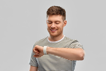 Image showing smiling young man looking at smart watch