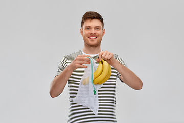 Image showing smiling man putting bananas into reusable net bag