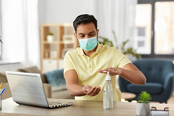 Image showing man in mask using hand sanitizer at home office