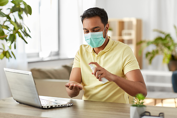 Image showing man in mask using hand sanitizer at home office