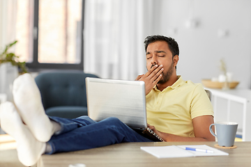 Image showing tired man with laptop and feet on table at home