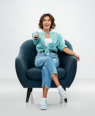 Image showing happy woman sitting in armchair with tv remote