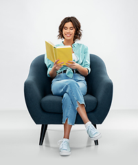 Image showing happy young woman in armchair reading book