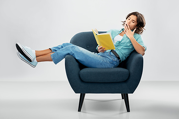 Image showing bored woman in armchair reading book and yawning