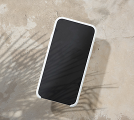 Image showing smartphone on beige color table top with palm leaf shadow