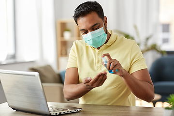 Image showing man in mask using hand sanitizer at home office