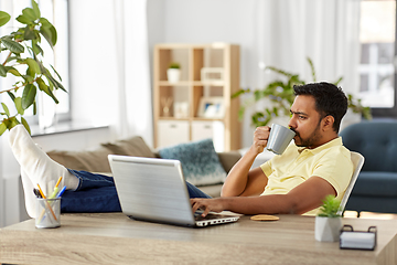 Image showing man with laptop drinking coffee at home office