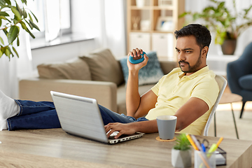 Image showing man with laptop and hand expander at home office