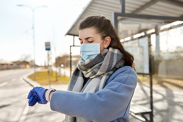 Image showing woman in mask looking at wristwatch at bus stop