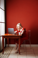 Image showing Young adult woman sitting at the table and working on laptop