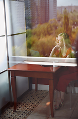 Image showing Young adult woman sitting at the table and working on laptop