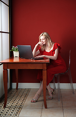 Image showing Young adult woman sitting at the table and working on laptop