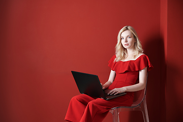 Image showing Young adult woman sitting on a chair and working on laptop