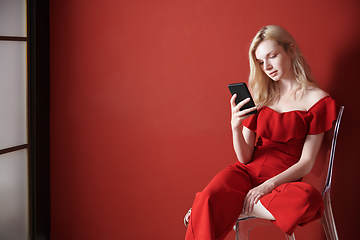 Image showing Young adult woman relaxing on a chair and using smartphone