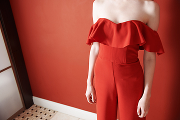 Image showing Young adult woman wearing red jumpsuit and standing next to the