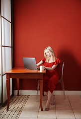 Image showing Young adult woman sitting at the table and working on laptop