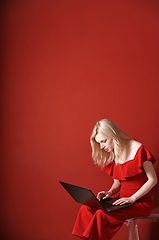 Image showing Young adult woman sitting on a chair and working on laptop