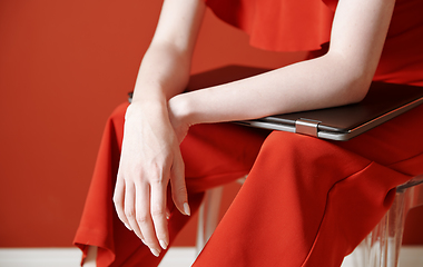 Image showing Young adult woman sitting on a chair and holding laptop